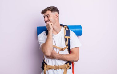 Genç ve yakışıklı bir adam mutlu ve kendinden emin bir ifadeyle gülümsüyor, elleri çenesinde. Yürüyüş konsepti