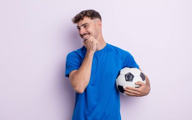 Genç ve yakışıklı bir adam mutlu ve kendinden emin bir ifadeyle gülümsüyor, elleri çenesinde. futbol kavramı