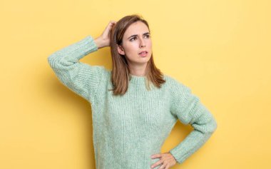 Genç güzel kız kafası karışmış ve kafası karışmış hissediyor, başını kaşıyor ve yan tarafa bakıyor.