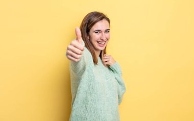 Genç, güzel bir kız gururlu, tasasız, kendinden emin ve mutlu, başparmağıyla olumlu gülümsüyor.