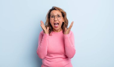 Orta yaşlı bir kadın beklenmedik bir sürpriz yüzünden şaşkın, heyecanlı, gülen, şaşkın ve mutlu hissediyor.