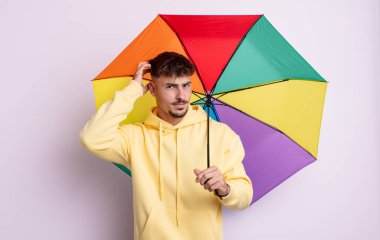 Kafası karışmış, kafası karışmış, kaşınan genç, yakışıklı bir adam. şemsiye kavramı