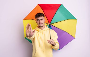 Genç ve yakışıklı adam ciddi görünüyor. Avuç içi gösteriyor. Durdurma hareketi yapıyor. şemsiye kavramı
