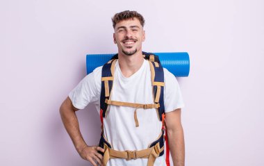 Genç yakışıklı adam mutlu bir şekilde gülümsüyor, eli kalçasında ve kendinden emin. Yürüyüş konsepti