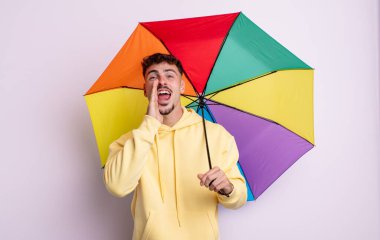 Genç yakışıklı adam mutlu hissediyor, elleri ağzının kenarında bağırıyor. şemsiye kavramı