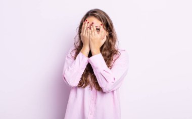 İspanyol güzel kadın elleriyle yüzünü kapatıyor, parmaklarının arasından şaşkın bir ifadeyle yan tarafa bakıyor.