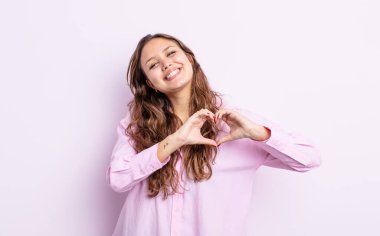 İspanyol güzel kadın gülümsüyor ve mutlu, sevimli, romantik ve aşık, iki eliyle kalbi şekillendiriyor.
