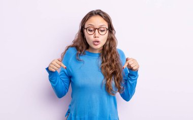 İki eliyle aşağıya bakan ağzı açık, şaşkın, şaşkın ve şaşırmış görünen İspanyol bir kadın.