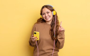 İspanyol güzel kadın gülümsüyor ve arkadaş canlısı görünüyor, bir numarayı gösteriyor. kulaklıklar ve akıllı telefon konsepti