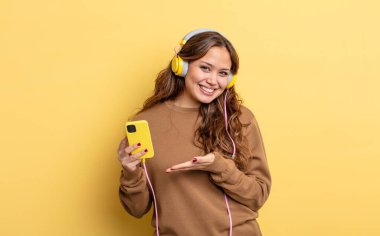 İspanyol güzel kadın neşeyle gülümsüyor, mutlu hissediyor ve bir konsept gösteriyor. kulaklıklar ve akıllı telefon konsepti