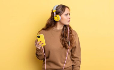 Profil görünümlü İspanyol güzel kadın hayal mi kuruyor, hayal mi kuruyor, hayal mi kuruyor? kulaklıklar ve akıllı telefon konsepti