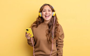 İspanyol güzel kadın mutlu ve hoş bir şekilde şaşırmış görünüyor. kulaklıklar ve akıllı telefon konsepti
