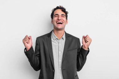 Genç işadamı son derece mutlu ve şaşırmış görünüyor, başarıyı kutluyor, bağırıyor ve zıplıyor.