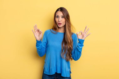 Asyalı güzel kadın şok olmuş, şaşırmış ve şaşırmış hissediyor. Onaylıyor. İki eliyle de onay işareti yapıyor.