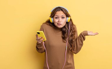 İspanyol güzel kadın şaşkın, şaşkın ve şüpheci hissediyor. kulaklıklar ve akıllı telefon konsepti