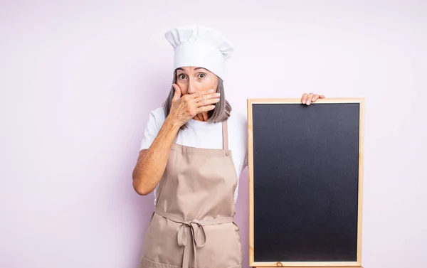 年长的漂亮女人用震惊的手捂住嘴 厨师和黑板的概念 — 图库照片