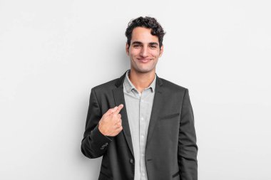 Genç işadamı gururlu, kendinden emin ve mutlu görünüyor, gülümsüyor ve kendini işaret ediyor ya da bir numaralı işareti yapıyor.