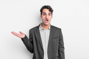 Genç işadamı şaşırmış ve şok olmuş görünüyor, çenesi düşmüş ve eli açık bir nesneyi tutuyor.