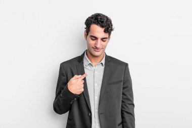 Genç işadamı neşeyle gülümsüyor, yere bakıyor ve göğsüne işaret ediyor.