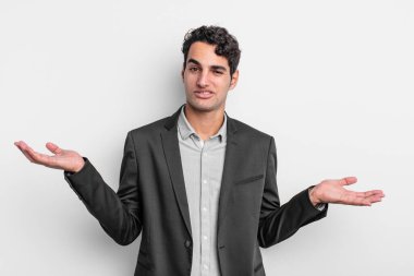 young businessman shrugging with a dumb, crazy, confused, puzzled expression, feeling annoyed and clueless
