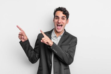 Genç işadamı kendini neşeli ve şaşırmış hissediyor. Şok olmuş bir ifadeyle gülümsüyor ve bir tarafı işaret ediyor.