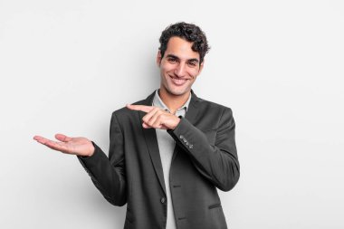 Genç işadamı neşeyle gülümsüyor ve yan taraftaki fotokopi alanına işaret ediyor, bir nesneyi gösteriyor veya reklamını yapıyor.