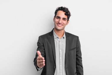 Genç işadamı gülümsüyor, mutlu, kendinden emin ve arkadaş canlısı görünüyor. Anlaşmayı bağlamak için el sıkışıyor, işbirliği yapıyor.