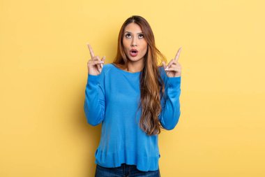 Asyalı güzel bir kadın şaşırmış, şaşırmış ve ağzı açık bir şekilde uzayı kopyalamak için iki elini havaya kaldırmış.