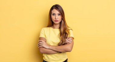 Asyalı güzel bir kadın hayal kırıklığına uğramış, hayal kırıklığına uğramış, ciddi görünüyor, kızgın ve kollarını kavuşturmuş.