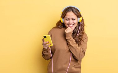 Mutlu, kendine güvenen, elleri çenesinde gülümseyen İspanyol güzel kadın. kulaklıklar ve akıllı telefon konsepti