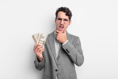 Ağzı ve gözleri açık, eli çenesinde İspanyol yakışıklı bir adam. iş ve dolar banknotları kavramı