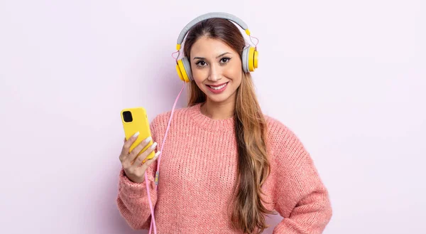 アジア系の可愛い女が喜んで手をつなぎ自信を持って笑ってる ヘッドフォンと電話のコンセプト — ストック写真