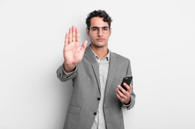 İspanyol yakışıklı adam ciddi görünüyor. Avuç içi gösteriyor. Durdurma hareketi yapıyor. iş ve telefon kavramı