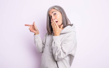 Yaşlı, güzel bir kadın mutlu, şok olmuş ve şaşırmış hissediyor. Ağzını eliyle kapatıyor ve yanal fotokopi alanını işaret ediyor.