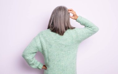 Son sınıf güzeli, kafası karışık ve bihaber bir kadın, bir çözüm düşünüyor, eli kalçasında, diğeri kafasında, dikiz aynasından.