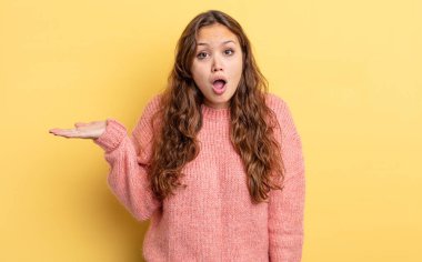 İspanyol güzel kadın şaşırmış ve şoka uğramış görünüyor, çenesi düşmüş, elinde açık bir elle bir nesne tutuyor.