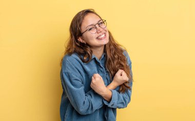İspanyol güzel kadın neşeli bir şekilde gülümsüyor ve kutluyor, yumruklarını sıkıp kollarını kavuşturuyor, mutlu ve pozitif hissediyor.