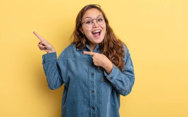 Hispanik güzel kadın neşeli ve şaşırmış hissediyor, şok olmuş bir ifadeyle gülümsüyor ve bir tarafı işaret ediyor.