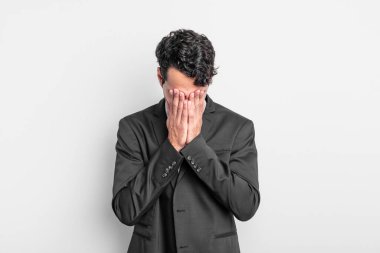 Genç işadamı üzgün, hayal kırıklığına uğramış, gergin ve depresif hissediyor. İki eliyle yüzünü kaplıyor, ağlıyor.