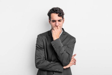 Genç işadamı kendini ciddi, düşünceli ve endişeli hissediyor. Elleri çenesine değmiş şekilde yan yan bakıyor.