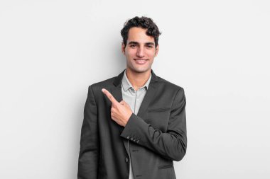 Genç işadamı neşeli bir şekilde gülümsüyor, mutlu hissediyor ve kenarı ve yukarıyı işaret ediyor, fotokopi uzayındaki nesneleri gösteriyor