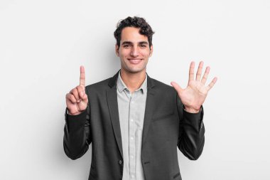 Genç işadamı gülümsüyor ve arkadaş canlısı görünüyor, 6 ya da 6 numarayı gösteriyor, elleri önde, geriye doğru sayıyor.