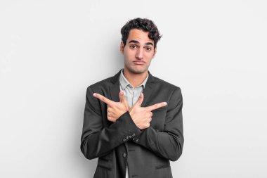 Genç işadamı şaşkın ve şaşkın görünüyor, güvensiz ve şüpheyle zıt yönleri işaret ediyor.