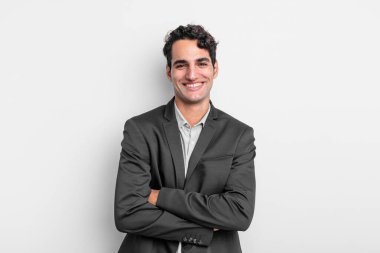 Genç iş adamı mutlu, gururlu ve tatmin olmuş görünüyor. Kollarını kavuşturup gülümsüyor.