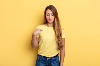 Asyalı güzel kadın neşeyle gülümsüyor, yere bakıyor ve göğsüne işaret ediyor.