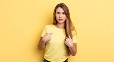 Asyalı güzel bir kadın şaşkın ve şaşkın bir bakışla kendini işaret ediyor. Seçildiğine şaşırmış ve şaşırmış.