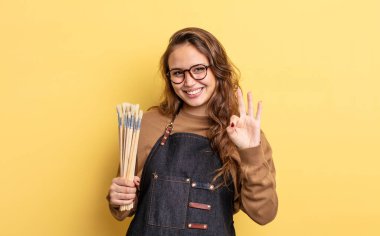 İspanyol güzel kadın gülümsüyor ve arkadaş canlısı görünüyor, üç numarayı gösteriyor. Fırça konsepti olan sanatçı