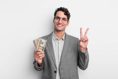 İspanyol yakışıklı adam gülümsüyor ve mutlu görünüyor, zafer ya da barış işareti yapıyor. iş ve dolar banknotları kavramı