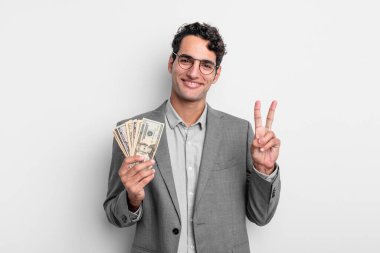İspanyol yakışıklı adam gülümsüyor ve arkadaş canlısı görünüyor, iki numarayı gösteriyor. iş ve dolar banknotları kavramı
