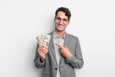 İspanyol yakışıklı adam neşeyle gülümsüyor, mutlu hissediyor ve bir tarafı işaret ediyor. iş ve dolar banknotları kavramı